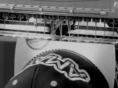 Black and White Image of Melco Embroidery Machine embroidering onto a cap