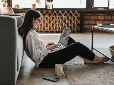 Woman sitting on floor against sofa with laptop looking happy