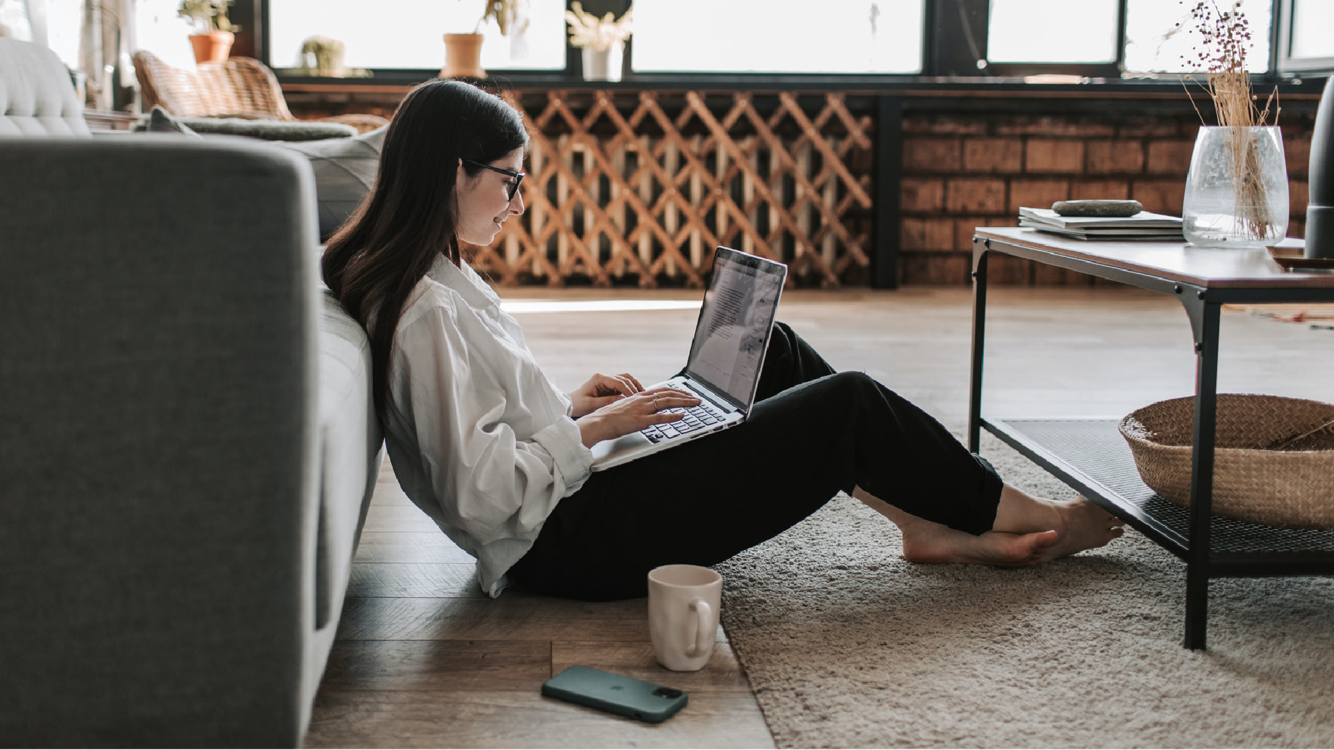 Woman sitting on floor against sofa with laptop looking happy