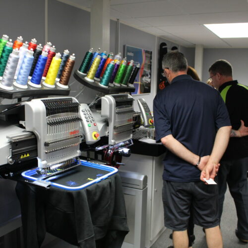 People looking at Melco EMT16X Embroidery machines in demo room